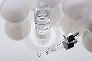 Cosmetic serum. Eyedropper with a drop and a bottle on a white mirror surface