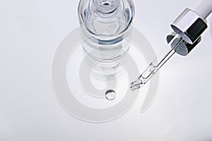 Cosmetic serum. Eyedropper with a drop and a bottle on a white mirror surface