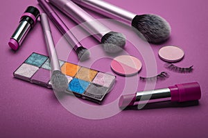 Cosmetic set of various shades compact and loose face powder, bronzed pearls, concealer and makeup brush on purple background.