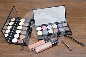 Cosmetic sets with eye shadows and brushes in black plastic case with mirror on wooden background