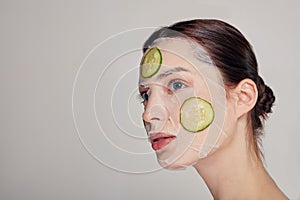 Close up gentle sophisticated girl in a moisturizing mask with a fresh cucumber on the face in the background looks away