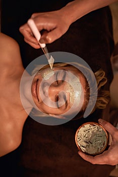 Cosmetician apply clay mask on woman face in spa
