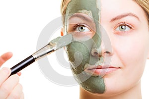 Cosmetician applying clay facial mask at woman face.