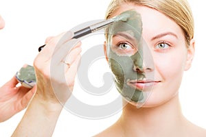 Cosmetician applying clay facial mask at woman face.