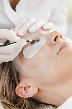 Cosmetician applying eyelash treatment to woman customer