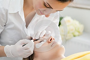 Cosmetician applying eyelash treatment to woman customer