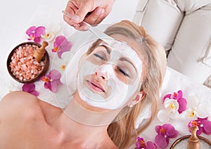 Cosmetician applying facial mask on face of woman