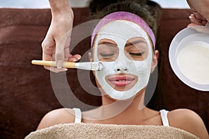 Cosmetician applying facial mask to the face of woman