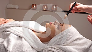 Cosmetician applying facial mask to the face of young woman in spa salon.