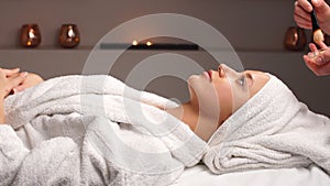 Cosmetician applying facial mask to the face of young woman in spa salon.
