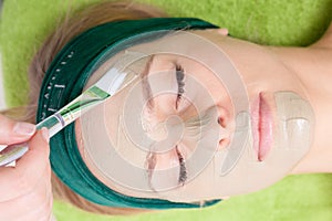 Cosmetician applying facial mask at woman face.