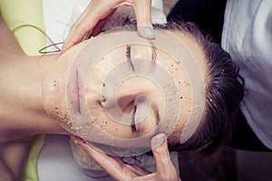 Cosmetician applying facial mask at young woman in spa salon