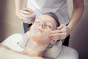 Cosmetician applying facial mask at young woman in spa salon