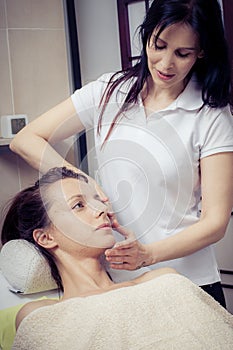 Cosmetician applying facial mask at young woman in spa salon