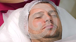 Cosmetician applying peeling to the face of young handsome man