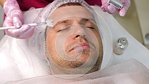 Cosmetician applying peeling to the face of young handsome man