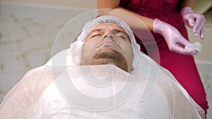 Cosmetician applying peeling to the face of young handsome man