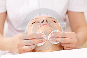 Cosmetician cleaning face using cotton pads