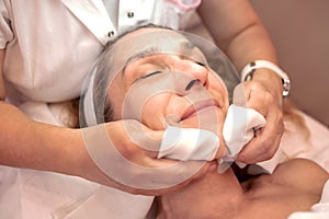 Cosmetician cleaning the surface of an older womanâ€™s face