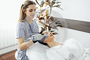 Cosmetician doing laser resurfacing to client in lying on couch in office