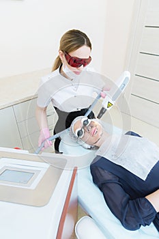 The cosmetician girl in goggles makes the procedure of carbon peeling with the help of a cosmetology laser. Carbon face