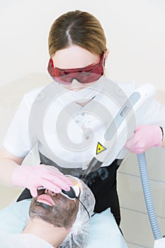 The cosmetician girl in goggles makes the procedure of carbon peeling with the help of a cosmetology laser. Carbon face