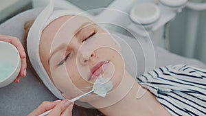 Cosmetician hands applying cream mask on young woman`s face at beauty spa salon