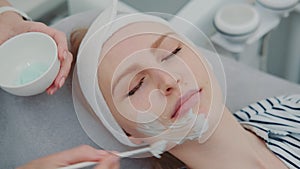 Cosmetician hands applying cream mask on young woman`s face at beauty spa salon