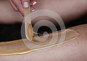 Cosmetician hands make depilation procedure on woman legs with wax