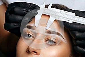 Cosmetician measuring brows before permanent makeup procedure