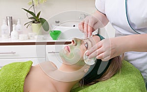 Cosmetician removing facial mask from woman face.