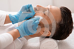 Cosmetician using blackhead remover for cleaning man face in spa