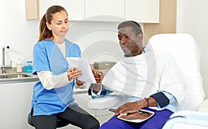 Cosmetician woman with papers talking to man before procedure in clinic