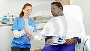 Cosmetician woman with papers talking to man before procedure in clinic