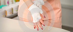 Cosmetician in workwear wearing white bamboo fingerless gloves on her hands in a beauty salon.