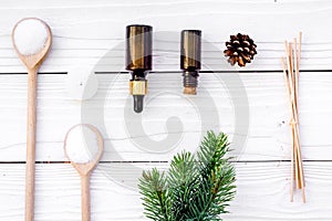 Cosmetics and aromatherapy concept. Pine spa salt, oil, pinecones and spruce branch on white wooden background top view