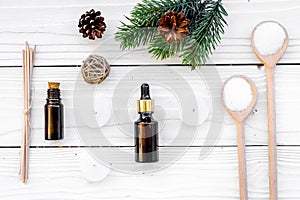 Cosmetics and aromatherapy concept. Pine spa salt, oil, pinecones and spruce branch on white wooden background top view