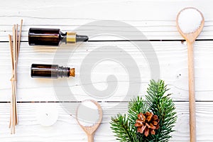 Cosmetics and aromatherapy concept. Pine spa salt, oil, pinecones and spruce branch on white wooden background top view