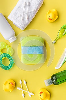 cosmetics for baby bath, towel and toys on yellow background top view pattern