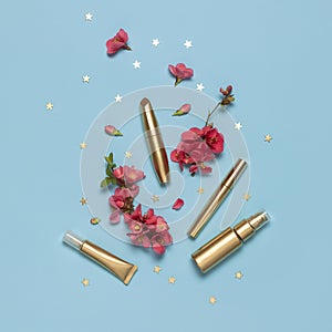 Cosmetics Branding Concept. Cosmetics, spring pink flowers, gold stars confetti on blue background. Cosmetic mock up gold bottles