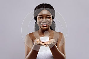 Cosmetics Concept. Beautiful smiling black lady holding white jar with moisturising cream