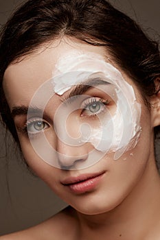 Cosmetics face care. Portrait of young brunette beautiful girl with face mask on well--kept skin posing over dark grey