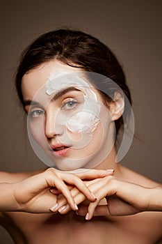Cosmetics face care. Portrait of young brunette beautiful girl with face mask on well--kept skin posing over dark grey