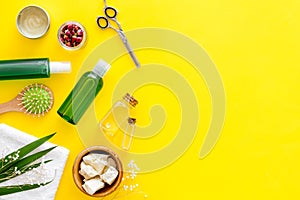 Cosmetics for hair with jojoba, argan or coconut oil in bottle, scissors, brush on yellow background top view mockup