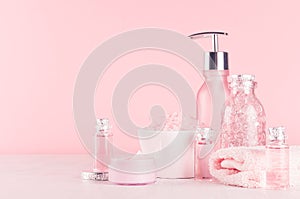 Cosmetics products for bath and spa - essential oil, bath salt, cream, liquid soap, towel in delicate pastel pink bath interior.