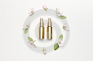 Cosmetics springtime Concept. Cosmetics, spring white flowers green leaves on light background. Cosmetic mock up gold bottles.