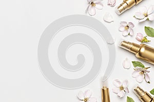 Cosmetics springtime Concept. Cosmetics, spring white flowers green leaves on light background. Cosmetic mock up gold bottles.