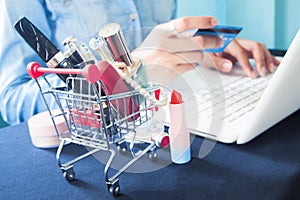 Cosmetics and woman`s essentials in shopping cart with woman usi