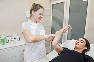 Cosmetologist applies sugar paste to the hand of a young woman.Depilation of female hands in a beauty parlor