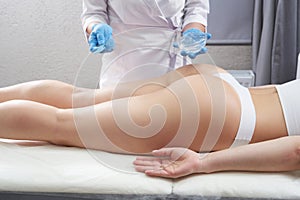 cosmetologist applies a transparent gel to the patient& x27;s legs and buttock for beauty treatment